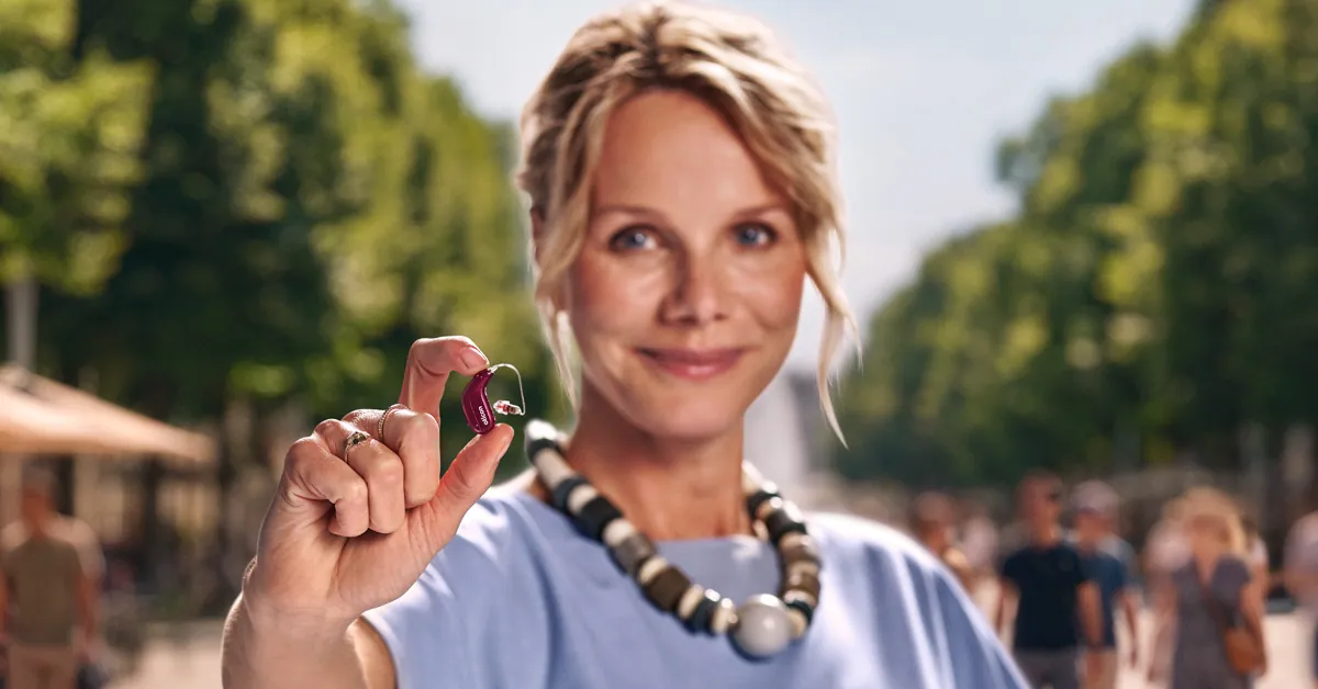 Woman holding a small Oticon Reveal hearing aid