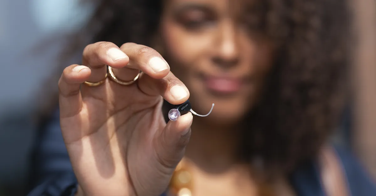 Woman holding a tiny Oticon Zeal hearing aid