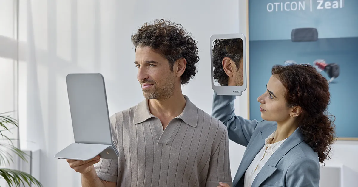 Hearing care professional showing a patient his discreet Oticon Zeal fit