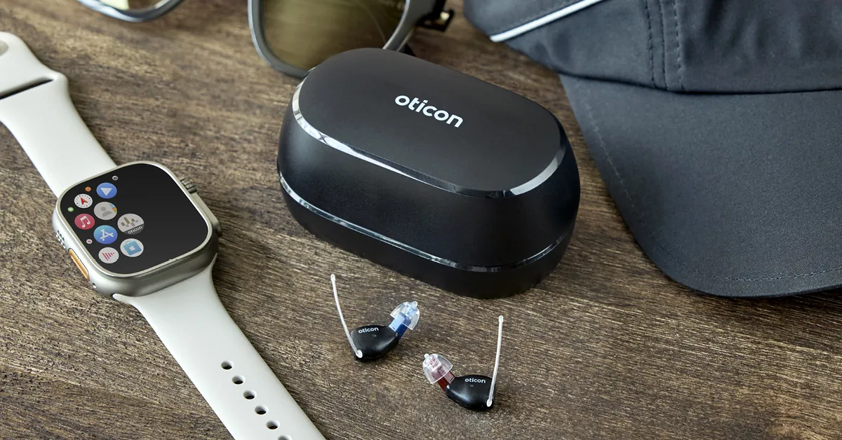 Oticon Zeal hearing aids and charger beside an Apple Watch